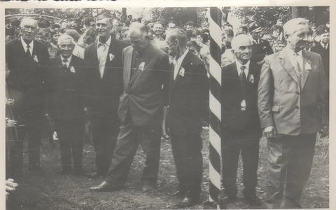 Archiwalne czarno-białe zdjęcie z obchodów 60-lecia: zasłużeni druhowie w garniturach z kotylionami, w tle mieszkańcy
