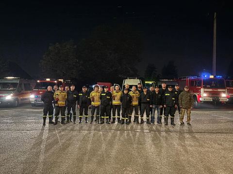 Druhowie OSP Skrzyszów ustawieni w szeregu przed wozami strażackimi, wieczorem, przed wyjazdem do działań powodziowych